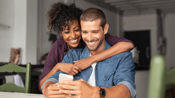 casal abraçado sorrindo olhando para celular